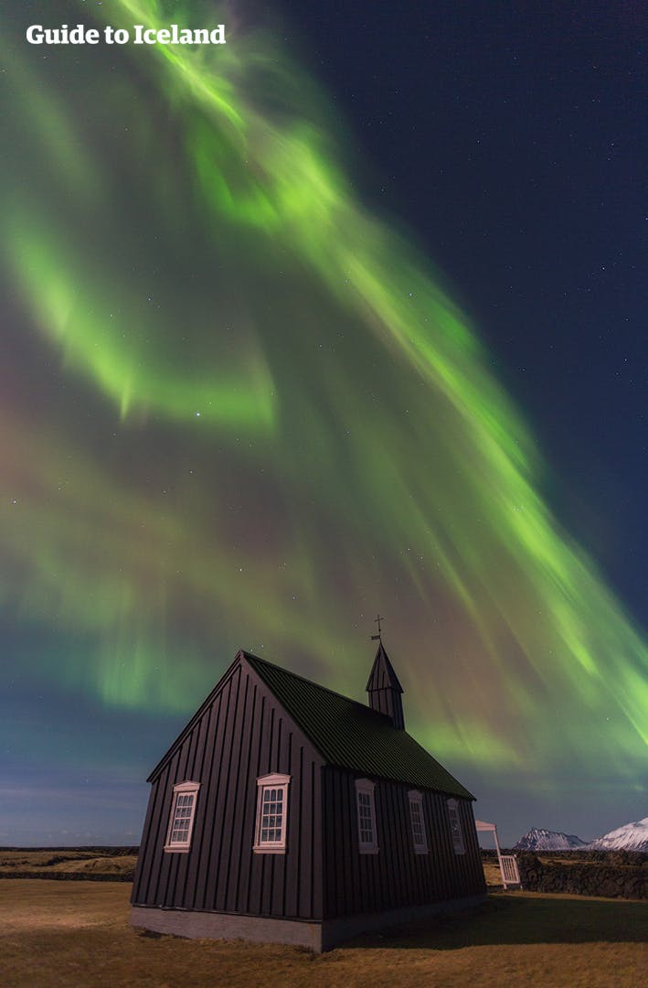 Fotogeniczny czarny Kościół w Búðir oświetlony przez zorzę polarną tańczącą na niebie.