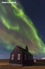 La photogénique église noire de Budir illuminée par les aurores boréales dans le ciel.