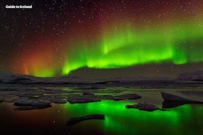 The dream-like northern lights shining green, yellow, and orange in the sky above the Jokulsarlon glacier lagoon in Iceland.
