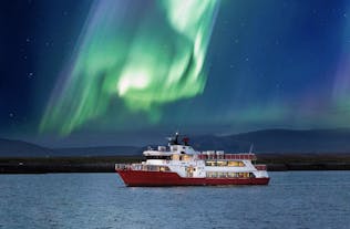 A red and white boat out in the Atlantic Ocean with northern lights above it.