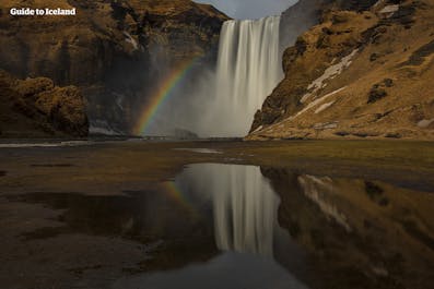 Der Wasserfall Seljalandsfoss mit einem Regenbogen, der durch die Reflexion der Sonne auf dem Wasser entsteht.