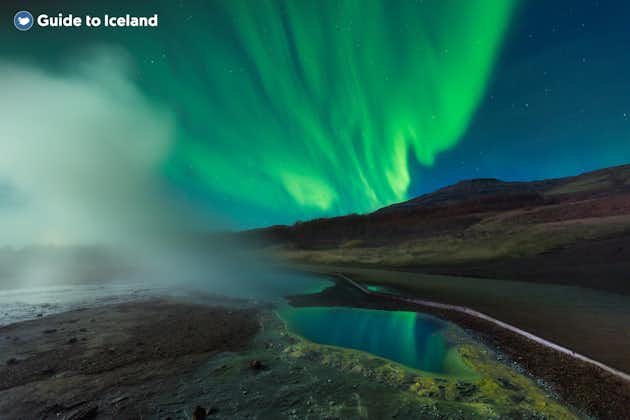 Eine Dampfsäule steigt in Island vor Nordlichtern auf.