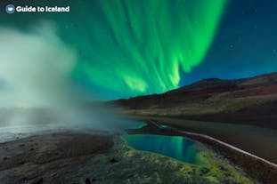 En dampsøyle stiger opp foran nordlyset på Island.