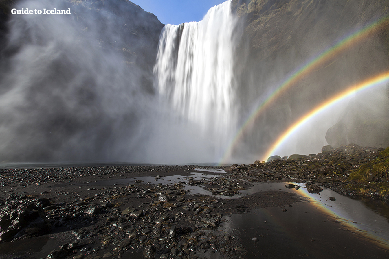 Skógafoss waterfall casting a rainbow as it lands on the black rocks below.