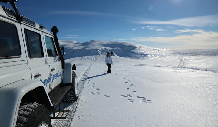 A person stands next to a super jeep on a snowy glacier in Iceland.