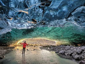 A woman stands inside an ice cave with crystal blue colors.