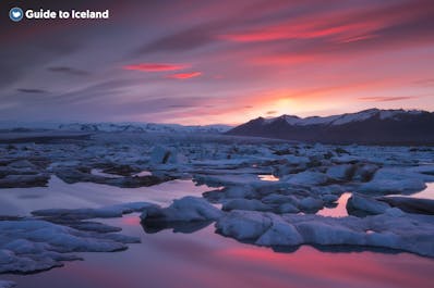 Niesamowity widok na lagunę lodowcową Jokulsarlon z zachodzącym słońcem tworzącym oszałamiające kolory na niebie.