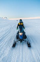 A person is seen standing on a snowmobile on top of a glacier.