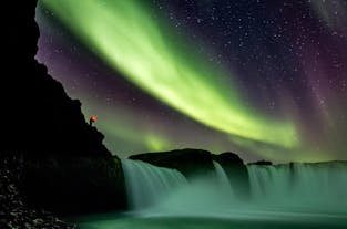 A display of aurora borealis dances above a waterfall in North Iceland.
