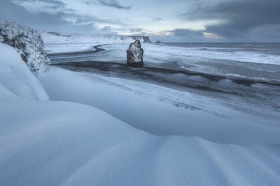 Het zwarte zandstrand van Reynisfjara, bedekt met een dikke sneeuwdeken in de wintermaanden