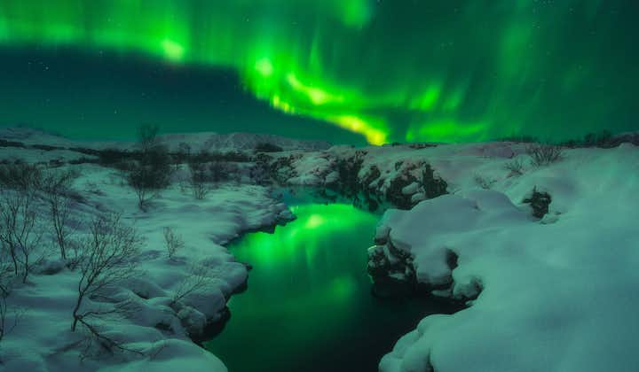 Zorza polarna na Islandii rozświetlająca śnieżną scenerię.