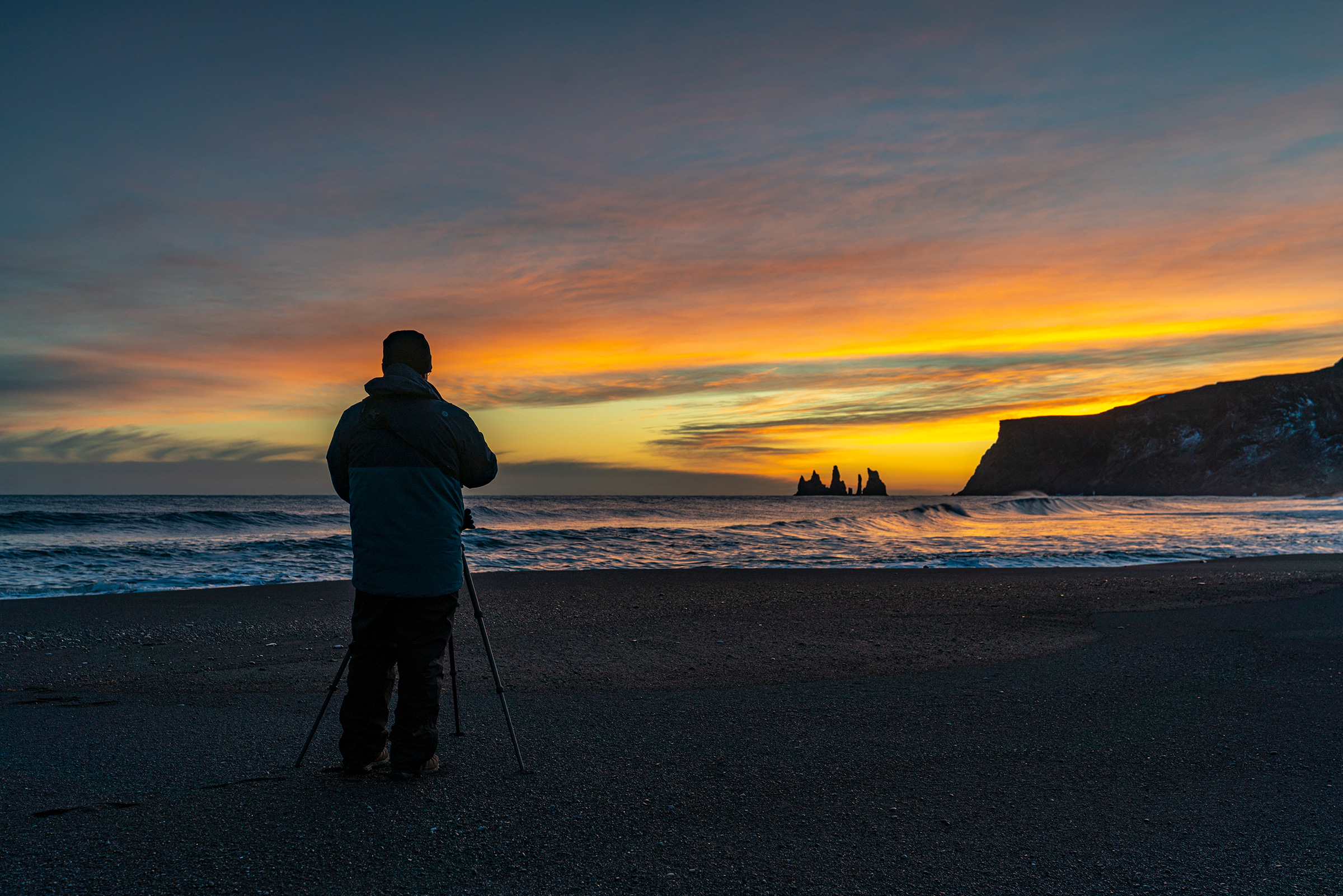 Reynisdrangar black sand beach with a man holding a camera in the foreground