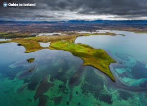 A picture taken from above of a lake and green moss with small houses in the North of Iceland. ri