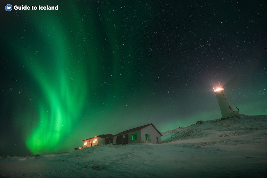 北极光在有房屋和灯塔的场景后闪闪发光