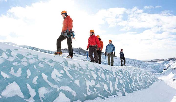 People wearing helmets, crampons, and warm clothing walk along a small ice ridge during a glacier hike in South Iceland.