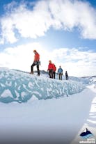 People wearing helmets, crampons, and warm clothing walk along a small ice ridge during a glacier hike in South Iceland.