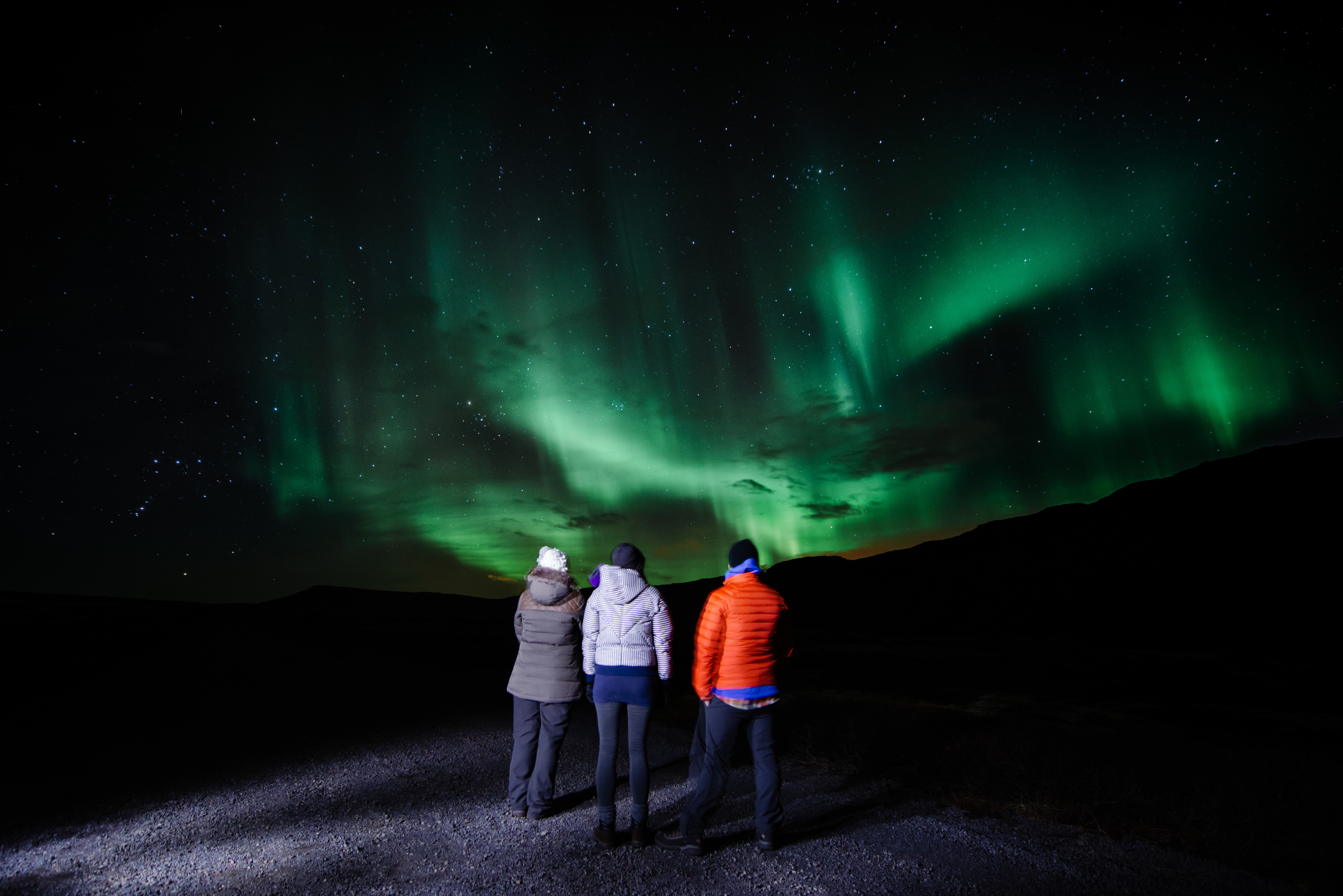 A group of three people standing looking up at the Northern Lights in Iceland