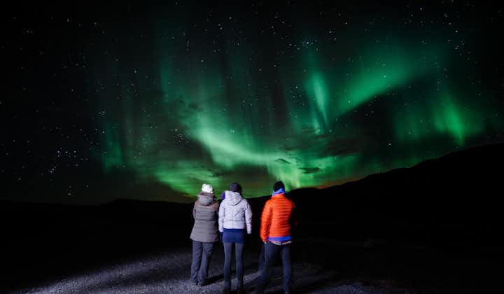 A group of three people standing looking up at the Northern Lights in Iceland