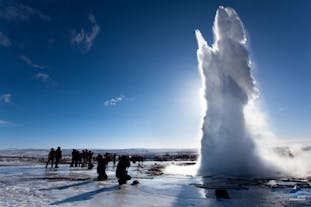 People watch as the Strokkur geyser erupts with an impressive display of water shooting high in the air in perfect contrast to the brilliant blue sky behind.