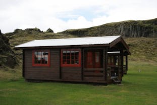 Side view of Holaskjol: Cabin 2, a wooden cabin with a porch.