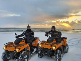 Two people on ATVs with a snowy landscape in the background.