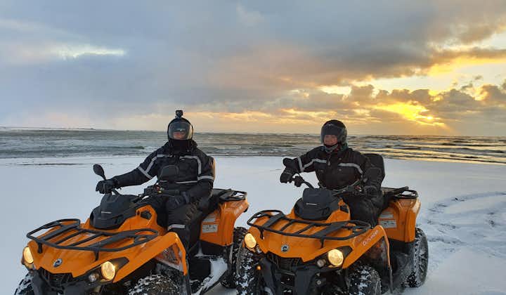 Two people on ATVs with a snowy landscape in the background.