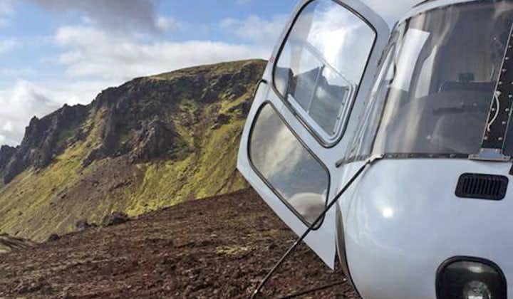 A helicopter with its door open on the edge of a crater in Iceland.