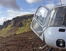 A helicopter with its door open on the edge of a crater in Iceland.