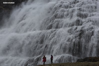 La cascada Dynjandi en los fiordos del oeste de Islandia, dos viajeros admiran las cataratas desde la base.