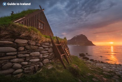 A turf house sitting at the edge of a lake at sunset in Iceland.