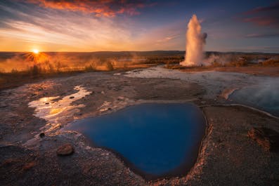 Zachód słońca nad wybuchającym gejzerem w obszarze geotermalnym Geysir słynnej trasy turystycznej Złotego Kręgu na Islandii.