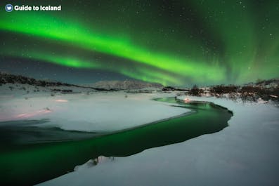 The aurora borealis appearing in the sky above a lake in Iceland in winter.