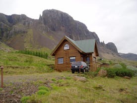 Wooden lodge with mountains in the background and a 4x4 vehicle parked in front of it.