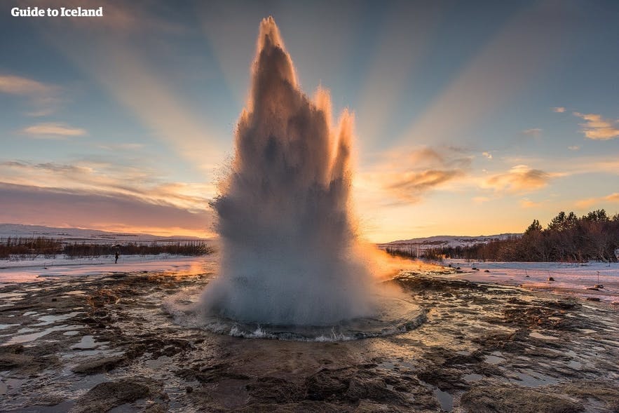 Geysir blasts steam against a backdrop of the winter sun.