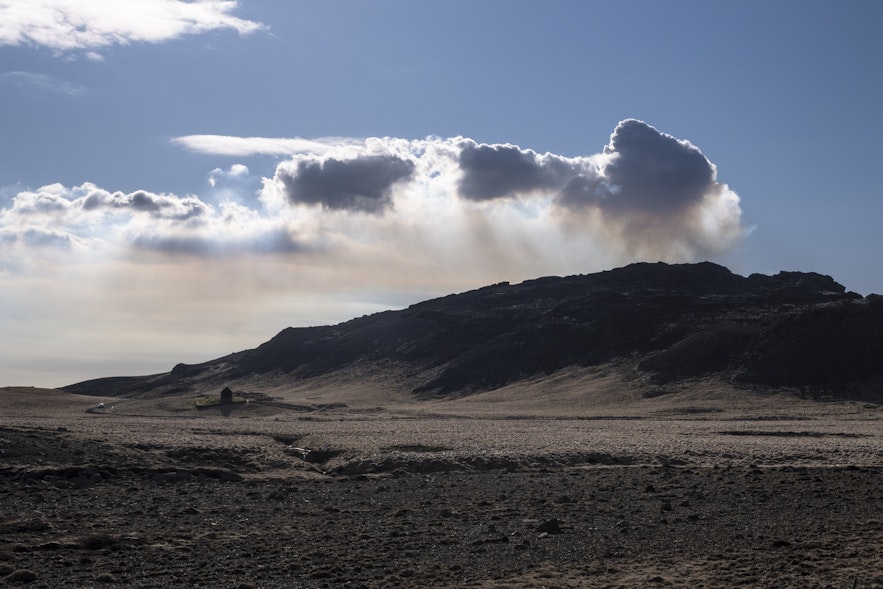 Aufsteigende Rauchwolken über dem Vulkan Fagradalsjall im Süden Islands mit der kleinen Kirche Krýsuvíkurkirkja.
