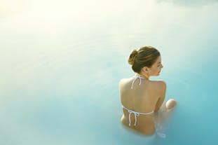 En kvinna sitter i vattnet i Blå lagunen.
