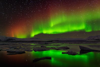 The northern lights shine green and pink in the sky above the Jokulsarlon glacier lagoon.