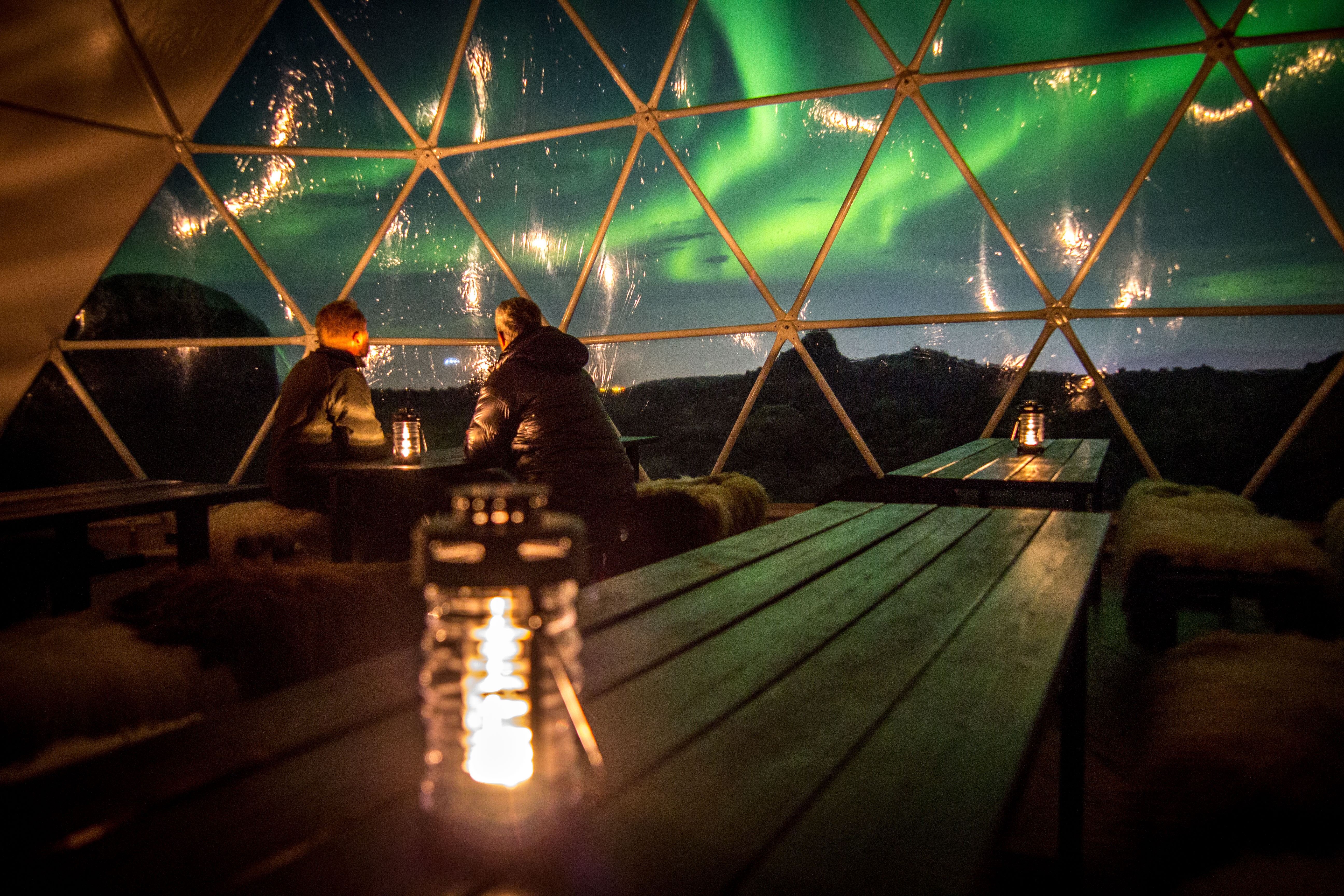 Two people watching the northern lights inside a geodesic dome at the aurora basecamp.