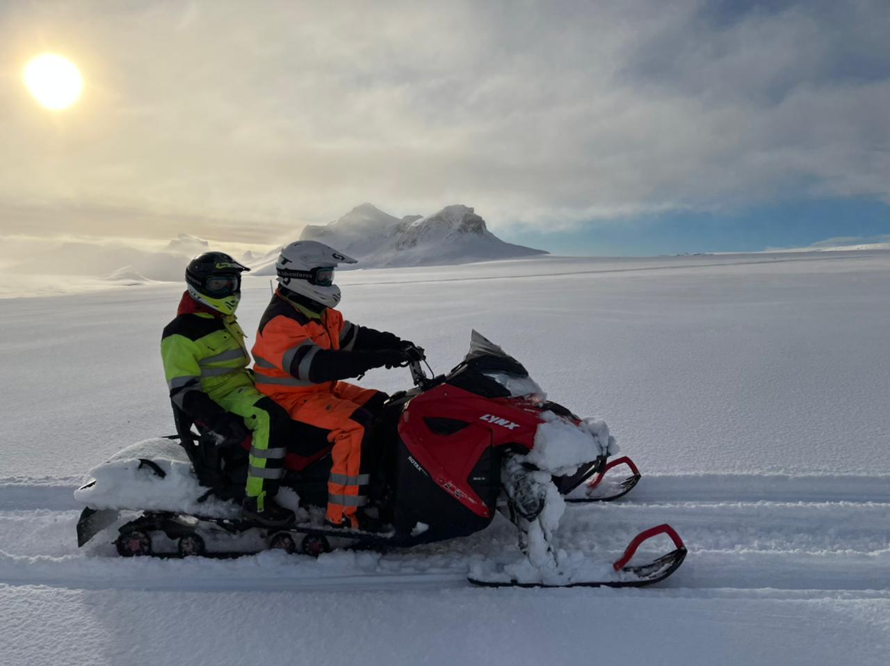 Two people riding on a snowmobile together on Langjokull glacier.