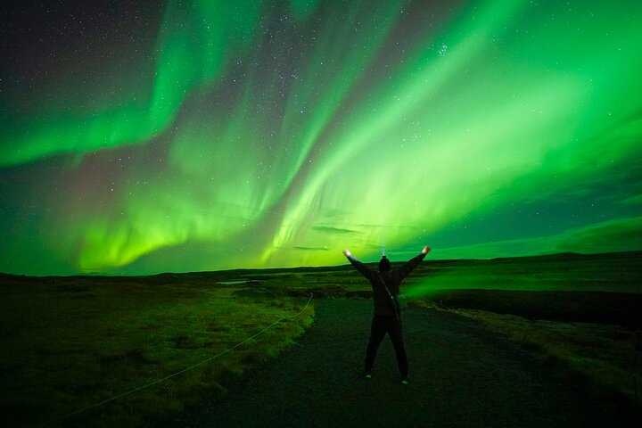 The northern lights in the sky above a person with their arms raised in celebration.