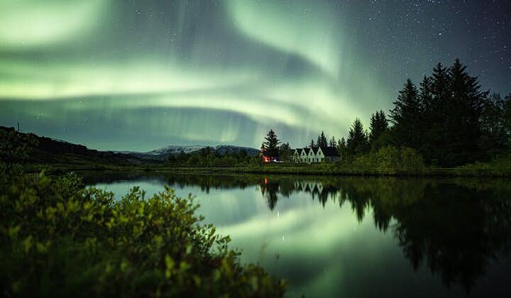The northern lights above a peaceful lake and a cottage.