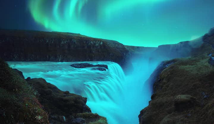 The northern lights appear in magical swirls of green above a beautiful waterfall in Iceland.