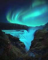 The northern lights appear in magical swirls of green above a beautiful waterfall in Iceland.