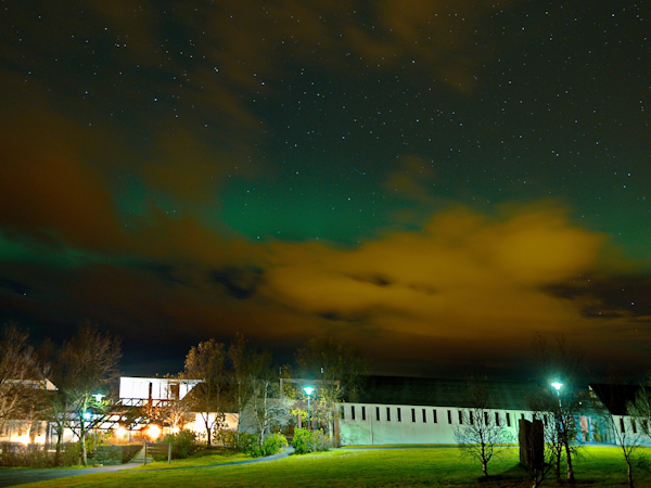 The aurora borealis above Hotel Skalholt on a cloudy, starry night.