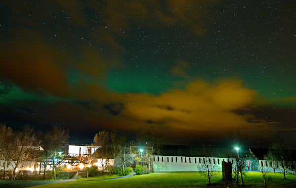 The aurora borealis above Hotel Skalholt on a cloudy, starry night.