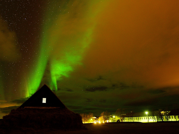 Pink and green colors from the aurora borealis light up the night sky above Hotel Skalholt.