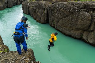 A person prepares to jump from the top of a rock on the Hvita river as they watch the person in front in mid-air.