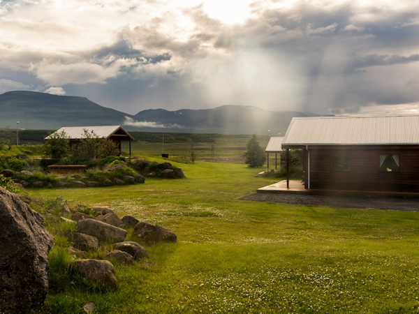 The countryside landscape at Hestasport Cottages with grass surrounding and the mountains behind.