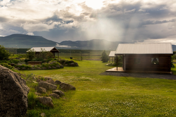 The countryside landscape at Hestasport Cottages with grass surrounding and the mountains behind.