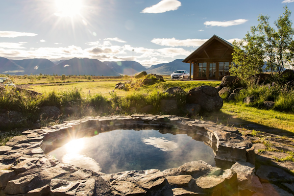 The natural outdoor hot tub at Hestasport Cottages with grass surrounding and mountains behind.